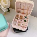 Joyero blanco abierto colocado sobre otros estuches cerrados con anillos y collares.