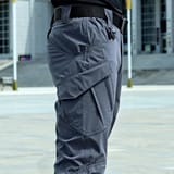 Acercamiento a la cadera y el muslo de un pantalón gris con cinturón negro rayado, de espaldas, en la calle frente a un edificio.