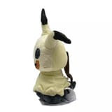 Vista de perfil del peluche de Mimikyu mostrando su cola marrón y etiqueta.