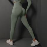 Modelo de espaldas usando mallas de entrenamiento color verde salvia con tenis blancos.