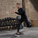 Hombre corriendo con ropa de compresión en una zona de entrenamiento con mancuernas.