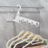 Percha blanca colgada de una barra metálica con varias perchas de plástico que sostienen toallas dobladas