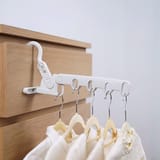 Percha blanca enganchada en el canto de un mueble de madera clara con cinco perchas y camisas blancas