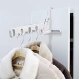 Percha blanca enganchada en el borde superior de una puerta o clóset blanco con abrigos colgados