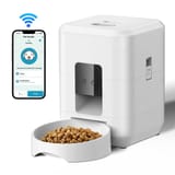 Comedero automático blanco con plato lleno de croquetas y teléfono mostrando la app de control.