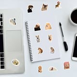 Escritorio con una libreta, laptop y taza con varias calcomanías de perros pegadas.