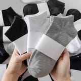 Dos manos sostienen tres calcetines con banda de papel, negro, blanco y gris, con un montón de calcetines envueltos al fondo.