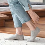 Persona sentada en el borde de una cama de madera, con calcetines tobilleros grises y pantalón de jean claro recortado.