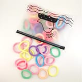 Ligas elásticas para el cabello en varios colores pasteles junto a una bolsa con cierre.