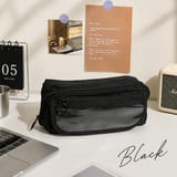 Estuche negro cerrado sobre un escritorio blanco, junto a un notebook, un calendario de escritorio y un parlante pequeño.