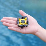 Dron amarillo posado sobre la palma abierta de una mano, con agua azul de fondo