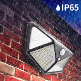 Luminaria solar negra inclinada sobre un muro de ladrillo rojo, con agua cayendo y gotas sobre los paneles de LED.