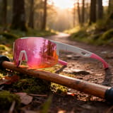 Gafas de montura blanca y luna rosa apoyadas sobre un bastón en un bosque.