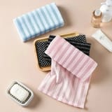 Toallas dobladas de color rosado, celeste y negro sobre una superficie plana, con una jabonera y envases de baño alrededor.