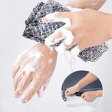 Manos llenas de espuma frotando una tira de cuadros sobre un antebrazo y, en un círculo pequeño, la tira bajo el chorro de una llave.
