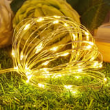 Rollo de alambre con luces micro LED doradas encendidas sobre pasto sintético.