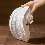 Una mano muestra la planta de la zapatilla de color crema con relieve en zigzag y perforaciones.