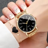 Mano femenina portando reloj dorado con esfera negra y pulsera con corazón negro.
