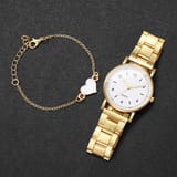 Reloj dorado con esfera blanca extendido junto a pulsera con corazón blanco sobre fondo negro.