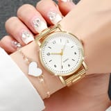 Mano femenina portando reloj dorado con esfera blanca y pulsera con corazón blanco.