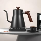 Tetera eléctrica negra sobre una mesa junto a una taza y una cafetera de goteo.