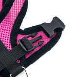 Acercamiento de la hebilla lateral de plástico negro abierta sobre la malla rosa del arnés.