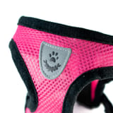 Acercamiento del parche gris en forma de escudo con huella, cosido sobre malla rosa con orilla negra.