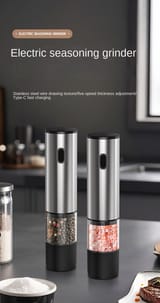 Dos molinillos automáticos cargados con pimienta y sal en grano sobre una encimera de cocina.