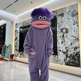 Persona con pijama enterizo morado de monstruo posando de frente en una sala de estar.