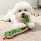 Perro blanco echado en una alfombra clara mordiendo y sujetando con las patas la serpiente de tela verde